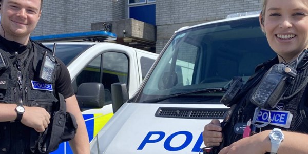 Two Police Officers standing infront of a stationary Police van