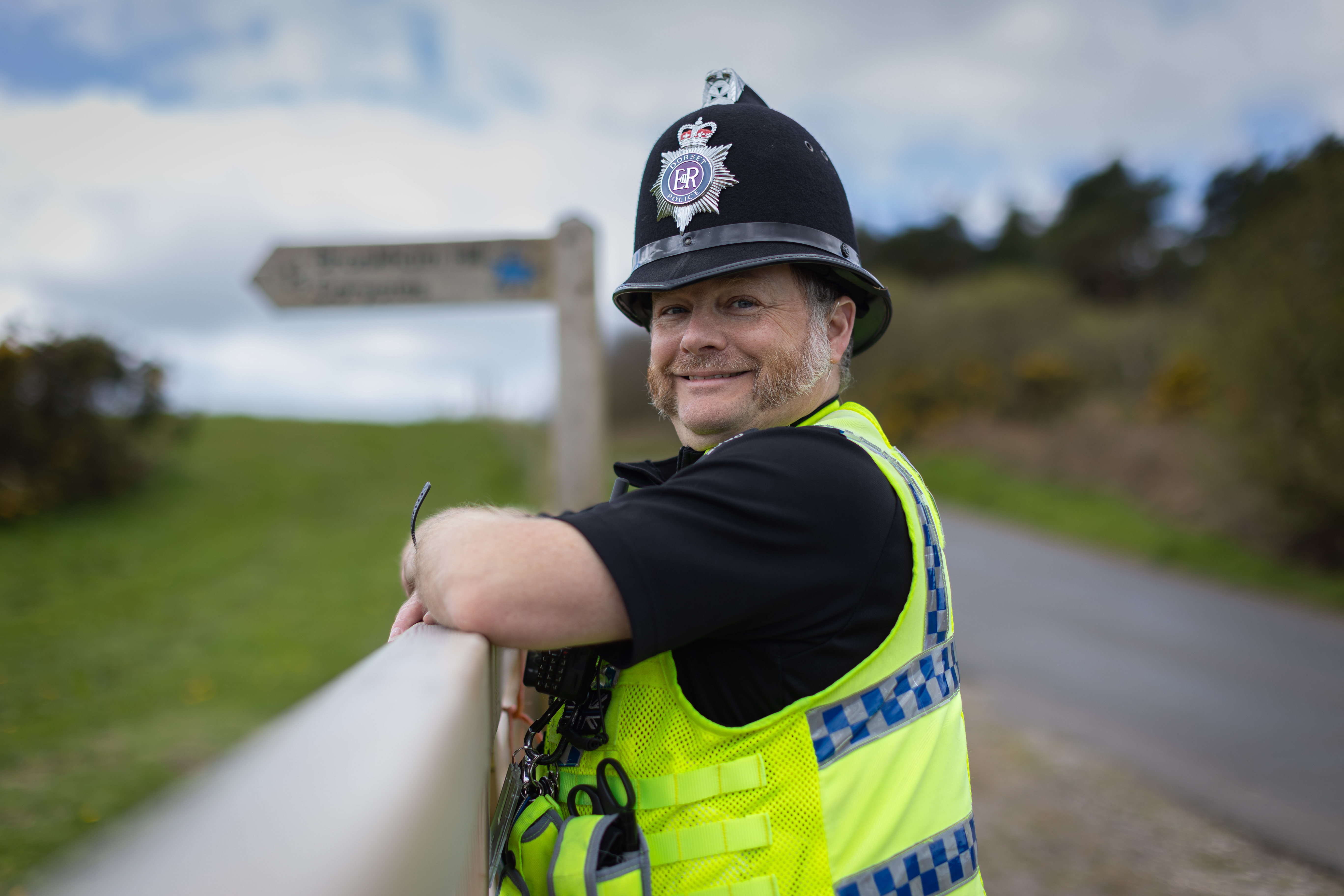 Male officer leaning on fence  beside country lane