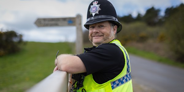 Male officer leaning on fence beside country lane