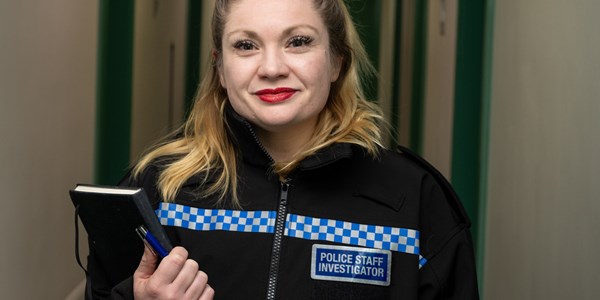 Women Police Staff Investigator in hallway holding an A4 sized notebook