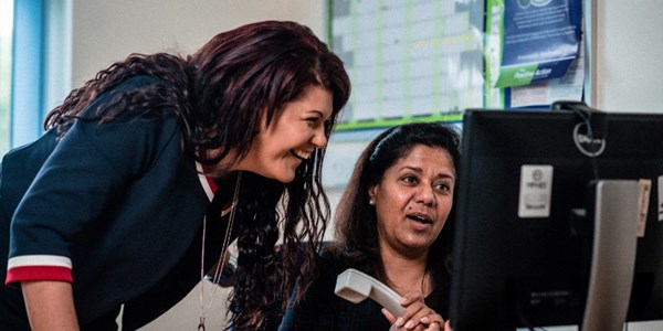 Two staff members smiling while looking at a monitor