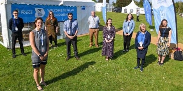 Staff members smiling standing in a field next to an event stand