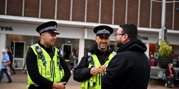 Two male special constables smiling speaking to a male shopper on Poole high street
