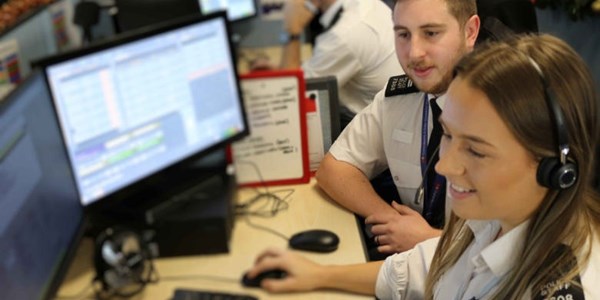 Two call handlers sat at a desk one with a headset on.